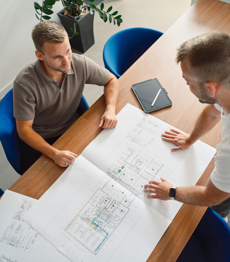 Zwei M&auml;nner stehen &uuml;ber Baupl&auml;nen an einem Tisch und besprechen Details.