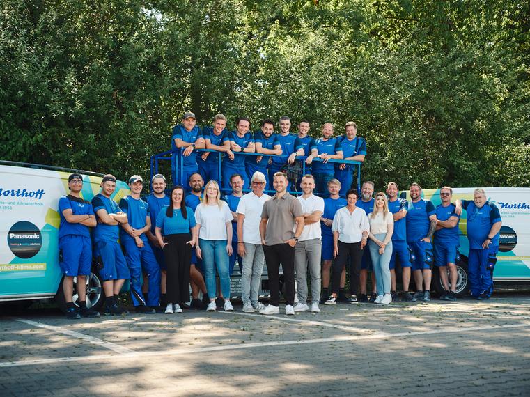 Großes Northoff Teamfoto mit vielen Mitarbeitern in blauer Kleidung vor Firmenvans.
