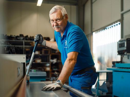 Ein älterer Northoff-Mitarbeiter in blauer Arbeitskleidung arbeitet an einer Metallbearbeitungsmaschine.