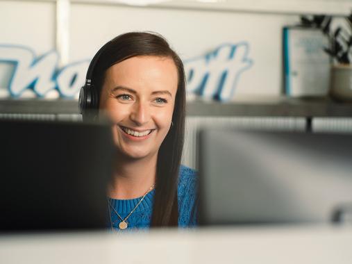 Eine lachende Northoff-Mitarbeiterin mit Headset arbeitet am Computer.