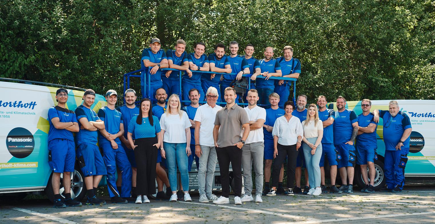 Großes Northoff Teamfoto mit vielen Mitarbeitern in blauer Kleidung vor Firmenvans.