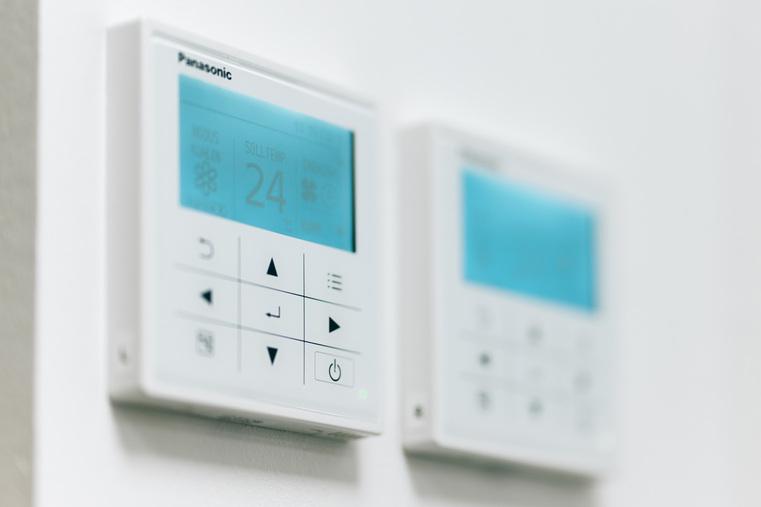 Zwei weiße Panasonic Thermostate an einer Wand, einer zeigt "24° Soll-Temp".