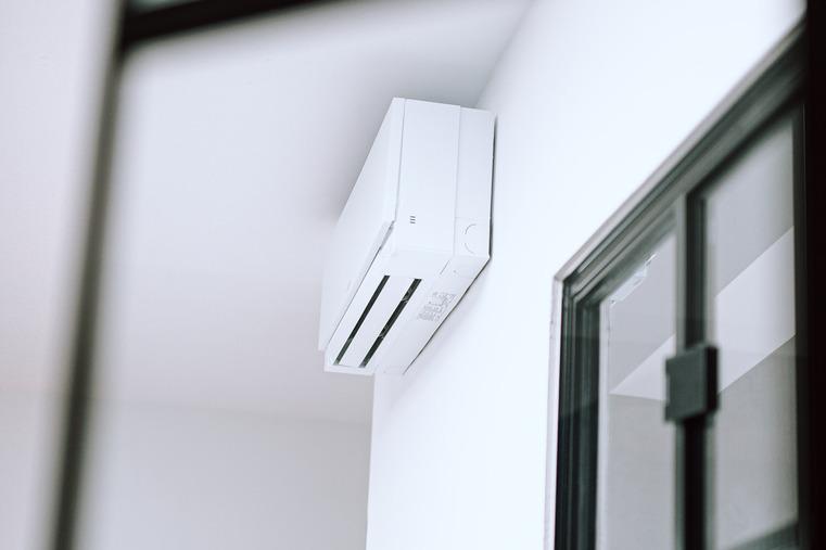 Weiße Klimaanlage an einer Wand in einem Raum, seitlich von einer Tür.