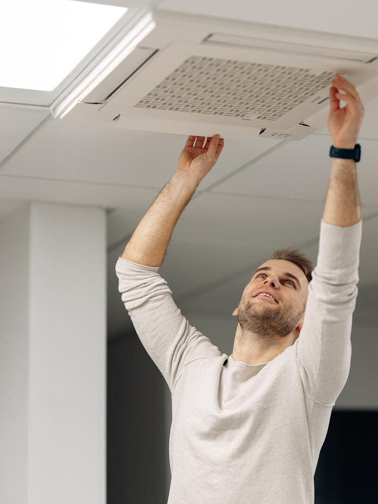 Techniker installiert oder wartet eine Deckenklimaanlage oder L&uuml;ftungseinheit in einem Innenraum.