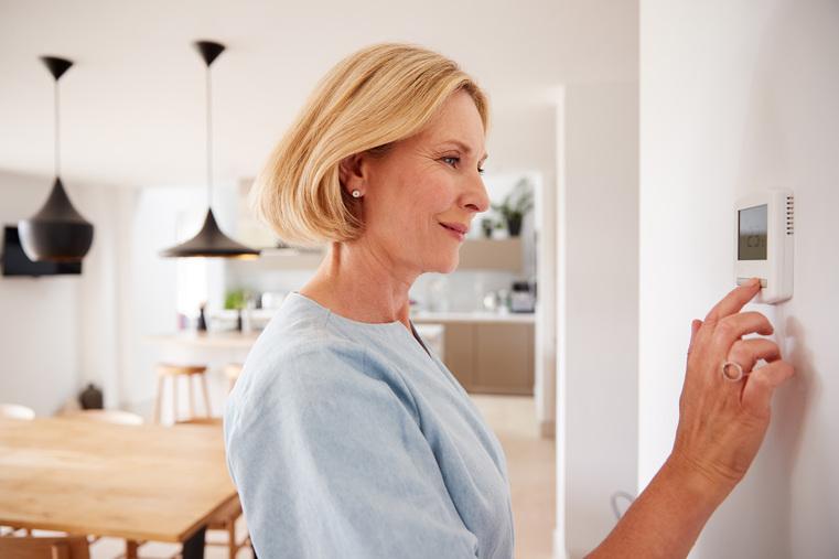 Frau stellt digitales Thermostat an der Wand ein. Klimatisierung und Raumklimasteuerung im Privathaushalt.