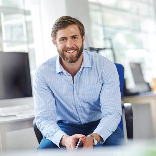 Lächelnder Geschäftsmann in Hemd sitzt im modernen Büro. Symbolisiert Klimasysteme für gewerbliche Büroräume.
