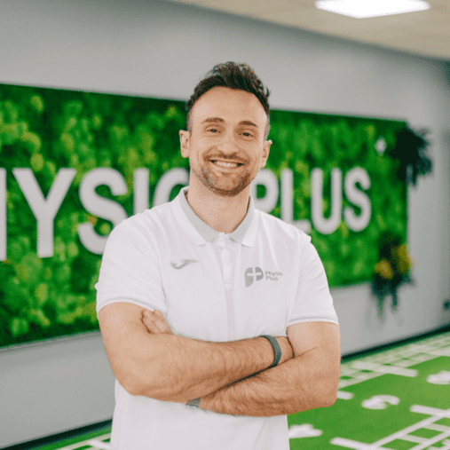 Trainer lächelt in Physiotherapie-Praxis mit Kunstrasen. Stellt Klimasysteme und Lüftungstechnik für Sportstätten dar.