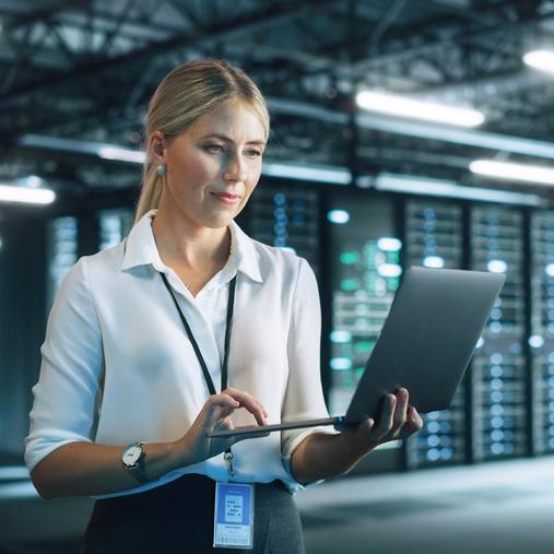 Frau nutzt Laptop in Serverraum mit leuchtenden Racks. Symbolisiert Präzisionsklimatisierung für Rechenzentren.