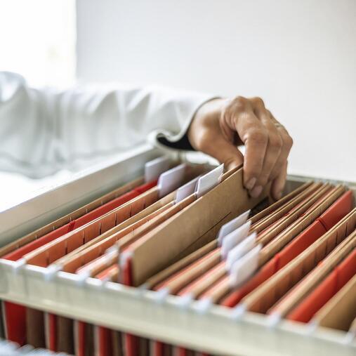 Hand greift in Aktenschrank mit Hängeregistern. Repräsentiert Klimatisierungslösungen für Büros und Verwaltung.