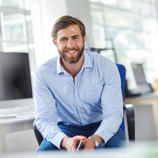 Lächelnder Geschäftsmann in Hemd sitzt im modernen Büro. Symbolisiert Klimasysteme für gewerbliche Büroräume.