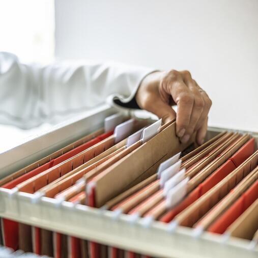 Hand greift in Aktenschrank mit Hängeregistern. Repräsentiert Klimatisierungslösungen für Büros und Verwaltung.